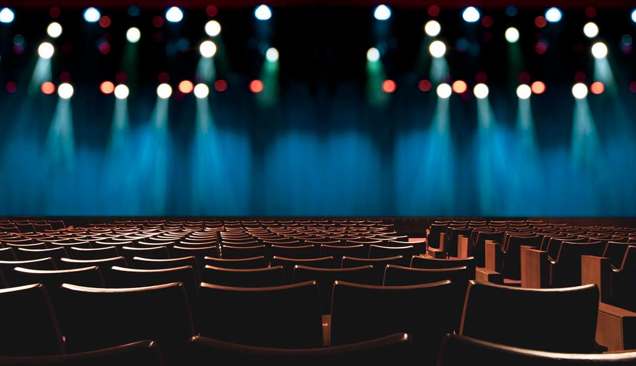 Sala de teatro con butacas de madera y luces de neón en el escenario