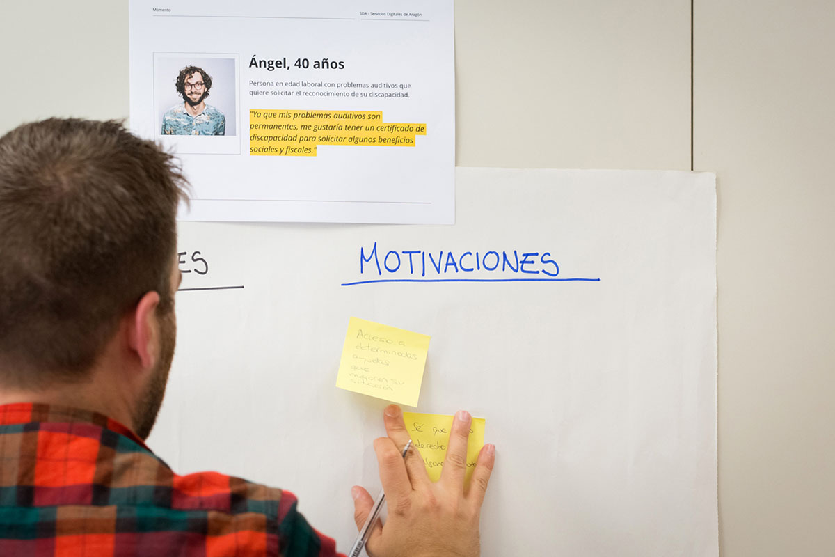 Un hombre pega un postit en una pizarra sobre la que hay un cartel que describe a un user persona